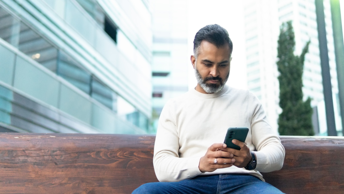 Mann benutzt sein Smartphone auf einer Bank