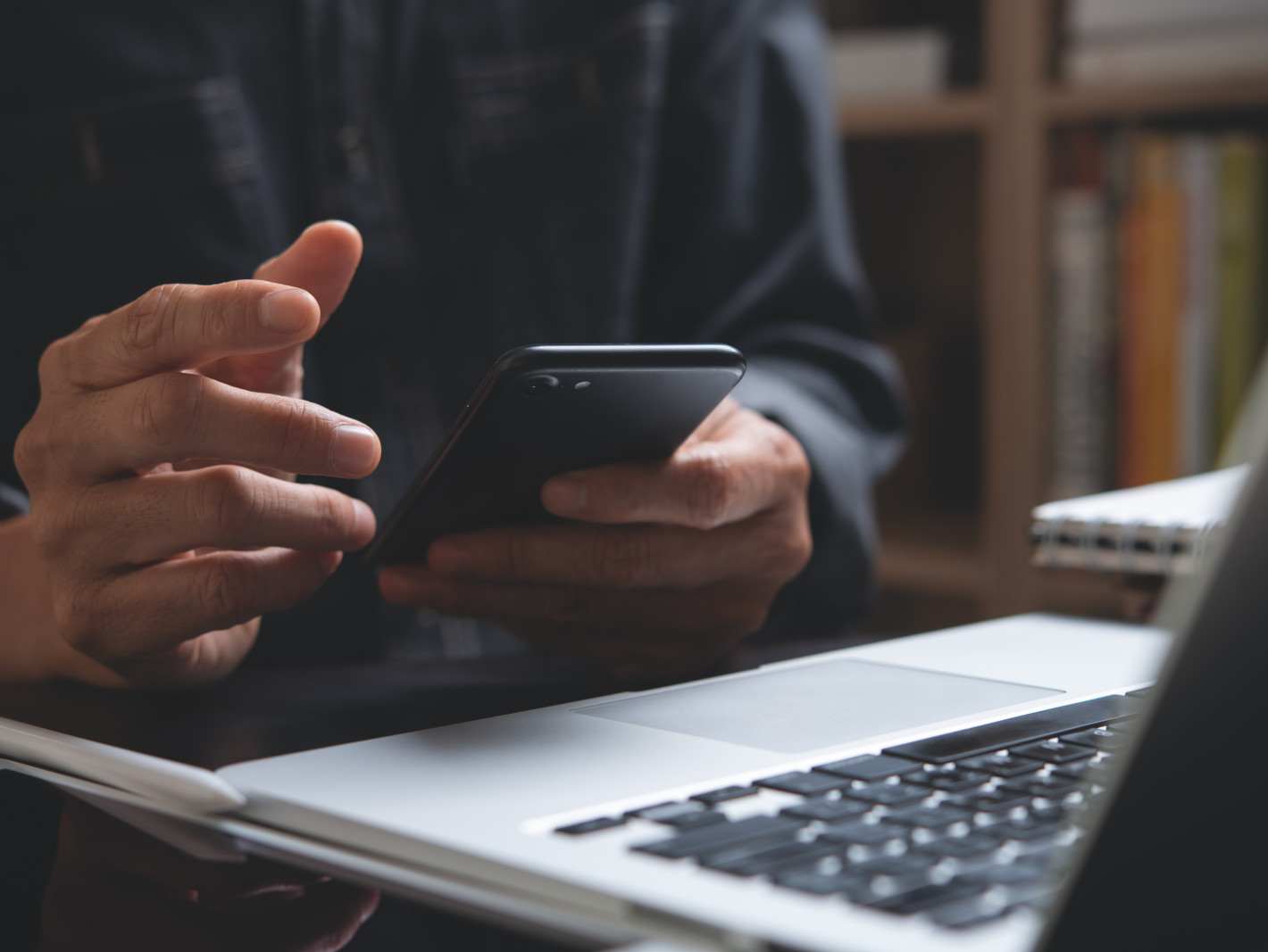 Mann prüft Handy vor Laptop