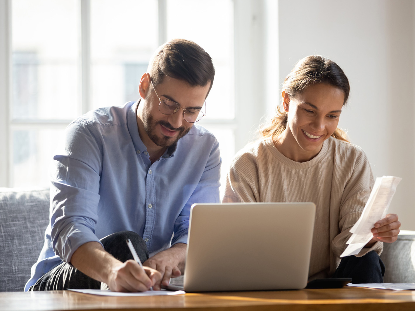 Ein Paar vor dem Laptop; er schreibt auf einen Zettel, beide lächeln