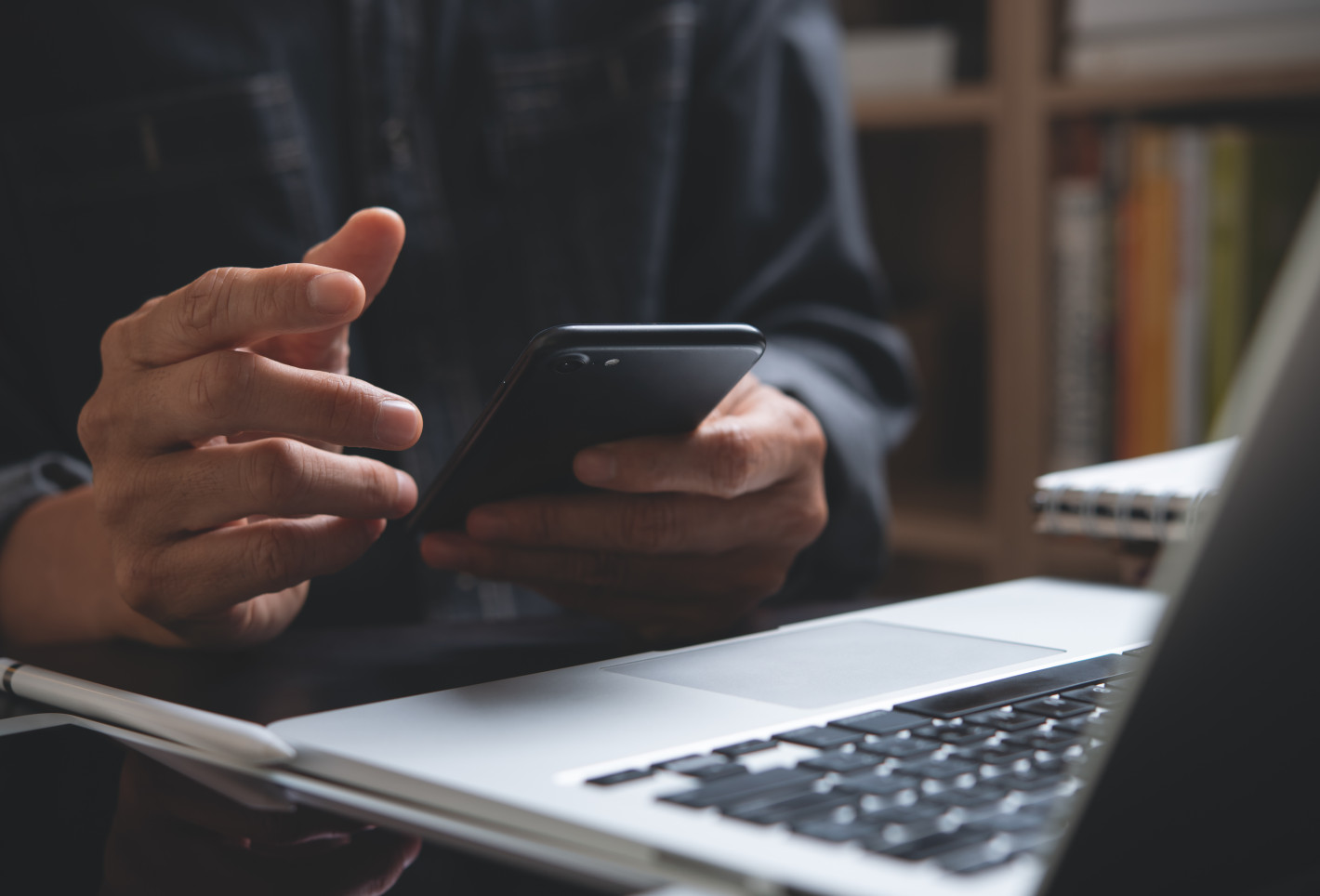 Mann prüft Handy vor Laptop